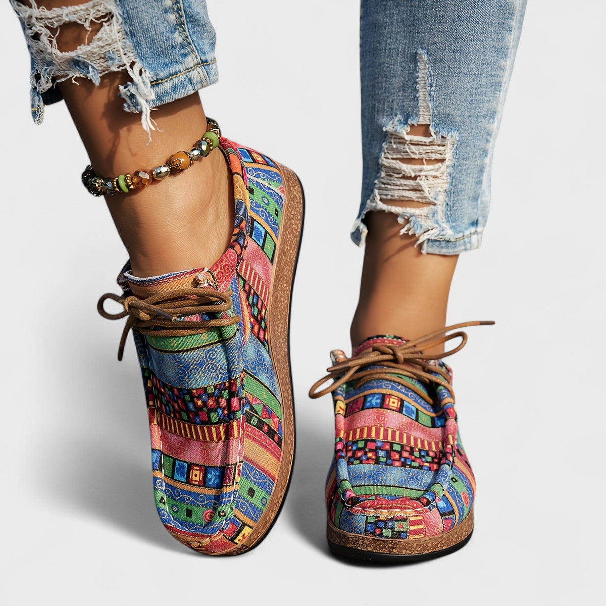Colorful patterned shoes worn with ripped jeans on a plain background